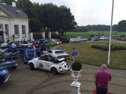 De zilveren Mustang Grande rijdt als onderdeel van een tourtocht met meerdere klassieke auto's en oldtimers door de historische binnenstad van Amersfoort, ter ere van een zakelijk jubileum.